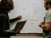 Two people mapping out a focused marketing plan on a whiteboard — planning the messages, channels and buyer stages that make up the 3-3-3 rule