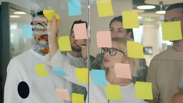 A team of marketers collaborating around sticky notes on a glass wall in a modern office — a fractional marketing team working together
