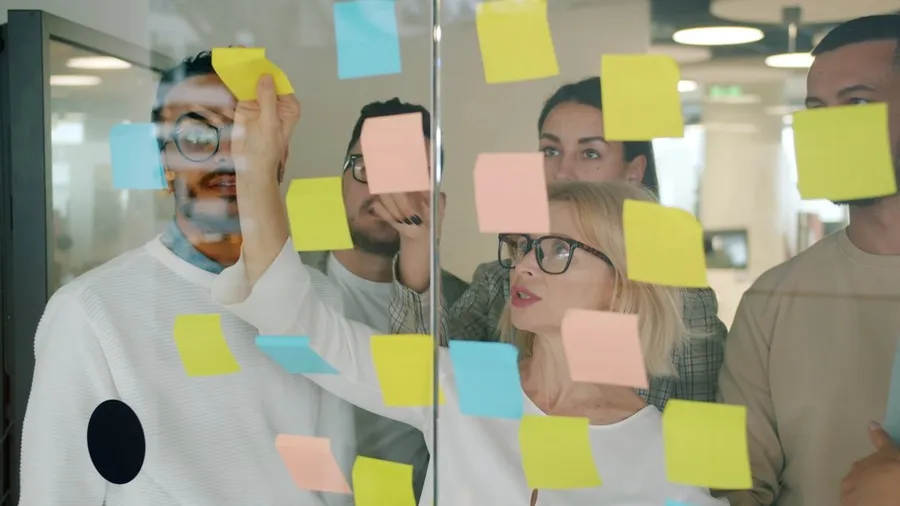 A team of marketers collaborating around sticky notes on a glass wall in a modern office — a fractional marketing team working together as one function