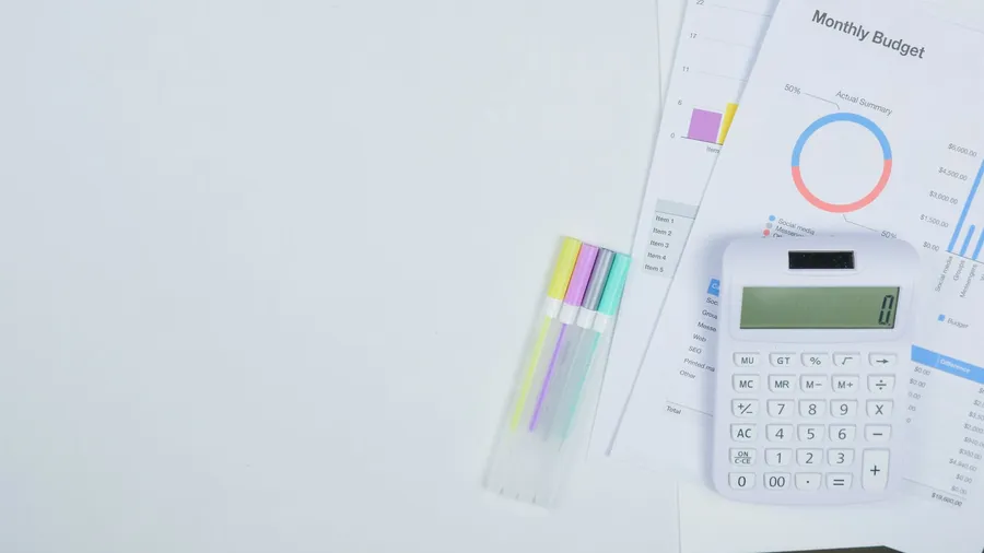 A small business owner at a desk comparing marketing outsourcing options, a laptop showing provider prices, a notepad with monthly figures, and a coffee, in a clean modern office