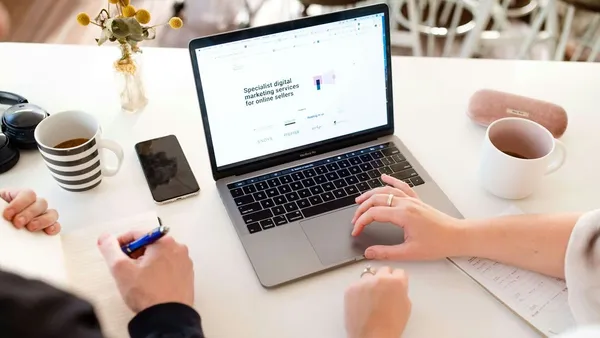 Two people reviewing a digital marketing services website on a laptop over coffee — weighing the cost of outsourcing marketing