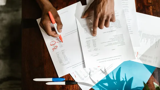 Overhead view of hands reviewing and highlighting a printed document at a desk — the human oversight that checks and approves AI marketing output before it ships