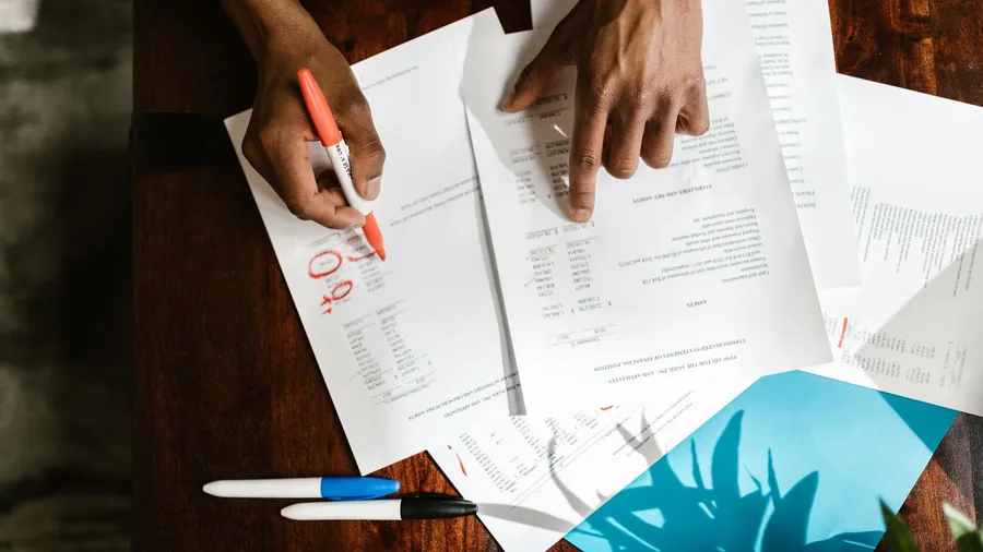 Overhead view of hands reviewing and highlighting a printed document at a desk, representing the human oversight that checks and approves AI marketing output before it ships