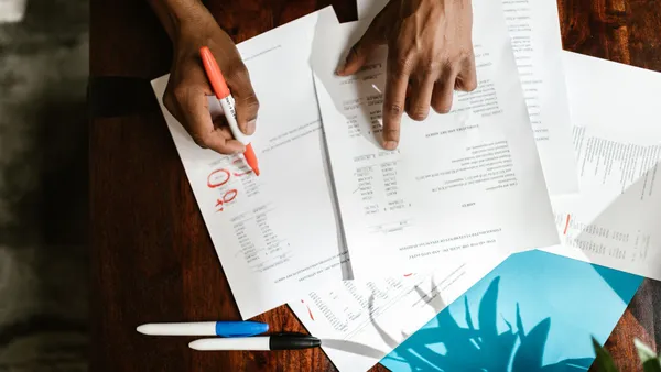 Overhead view of hands reviewing and highlighting a printed document at a desk — the human oversight that checks and approves AI marketing output before it ships