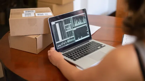A small business owner reviewing sales charts on a laptop at a table surrounded by shipping boxes — figuring out what actually works in small business marketing