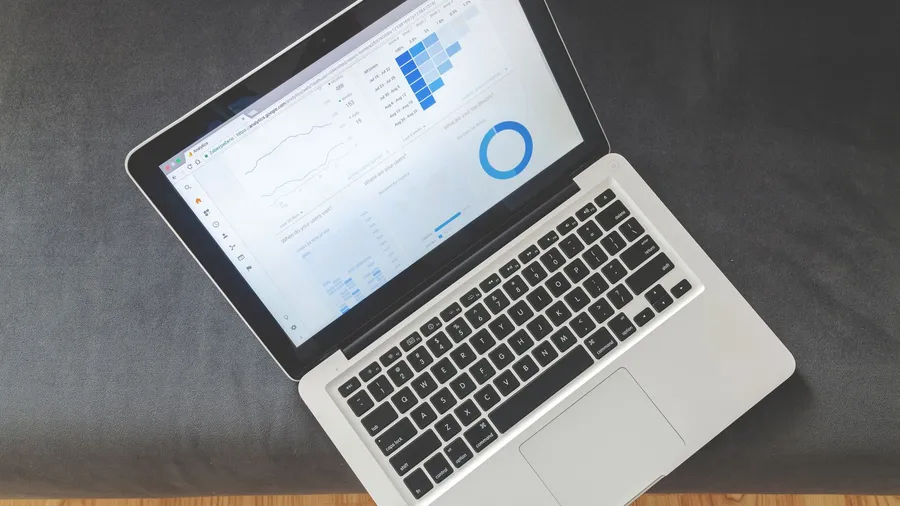 Small business owner checking marketing analytics dashboard on a laptop next to shipping boxes, tracking marketing results over time